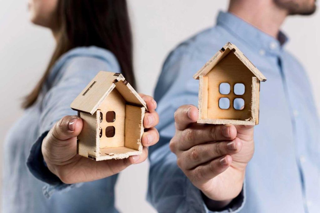 A separated couple each holding a miniature house, representing the division of assets and property in family law disputes managed by Judith Ramos, Attorney at Law in Miami, Florida.