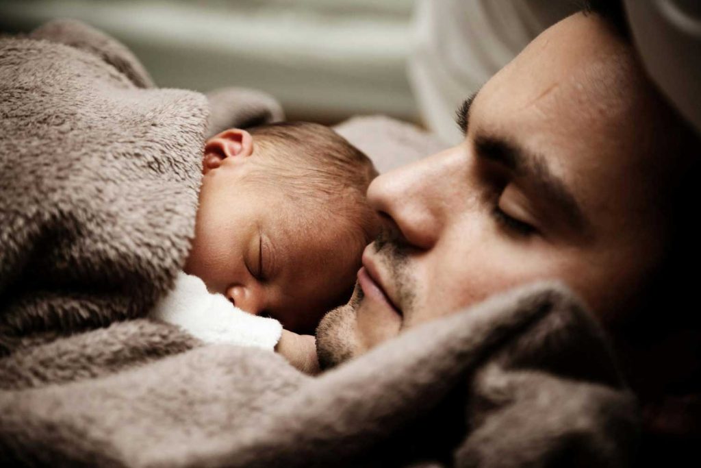 A tender moment with a father sleeping next to his newborn baby, representing the close bond and responsibility in fatherhood, an important element in family law cases managed by Judith Ramos, Attorney at Law in Miami, Florida.