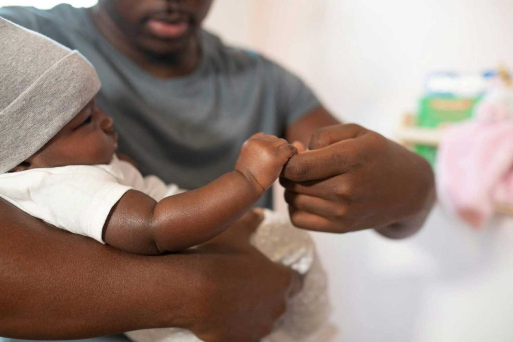 A father gently holding his baby’s hand, representing care and paternal love in father’s rights and paternity cases managed by Judith Ramos, Attorney at Law in Miami, Florida.
